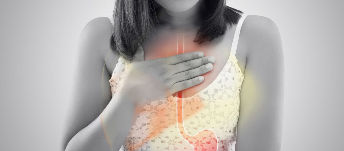 Woman suffering from Acid reflux or Heartburn against gray background / Asian people with symptomatic Indigestion or Gastritis